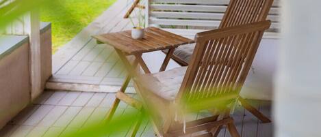 A wooden deck with two chairs and a table, surrounded by white blinds.