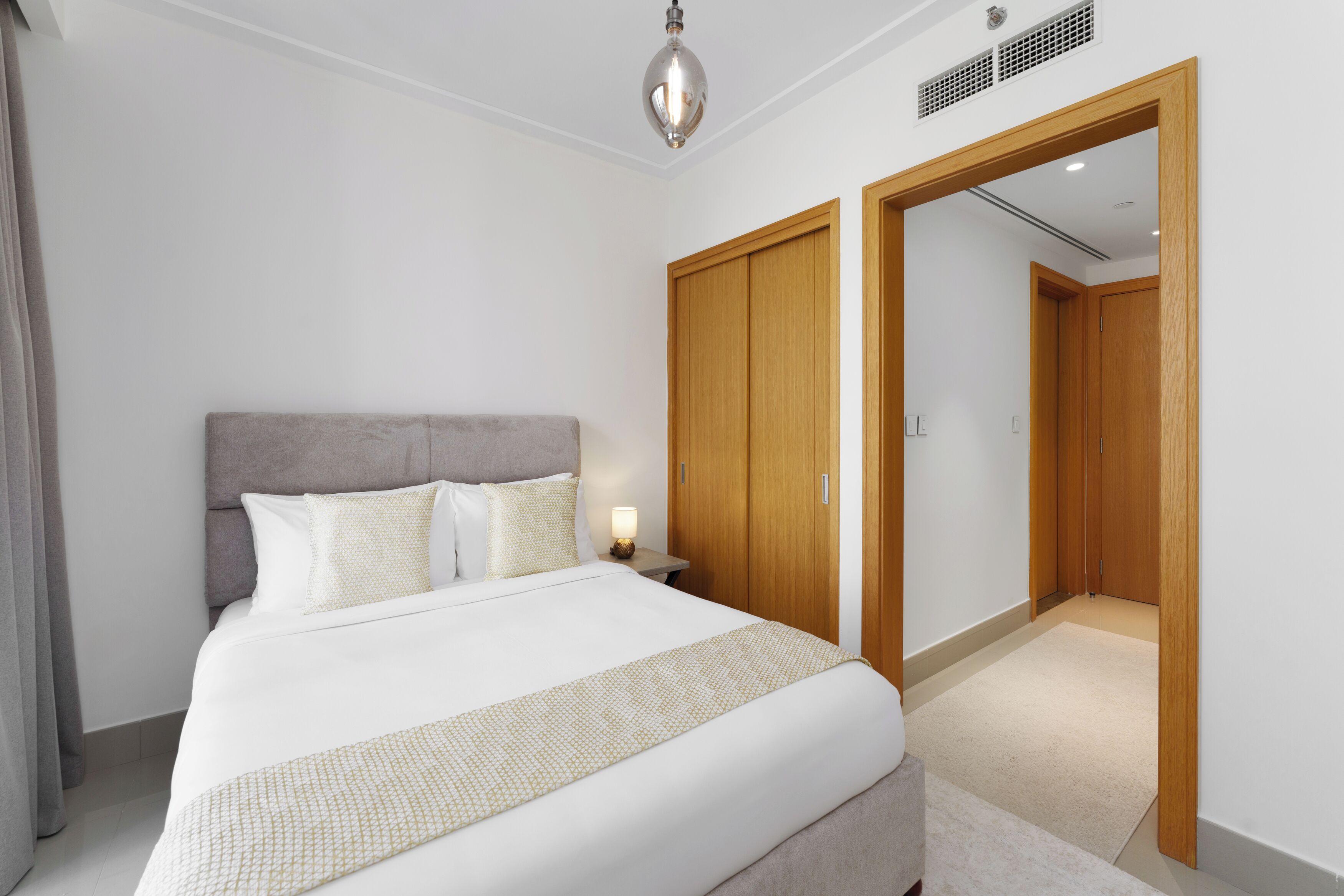 Habitación de hotel con una cama grande, un armario de madera y una mesita de noche con lámpara.