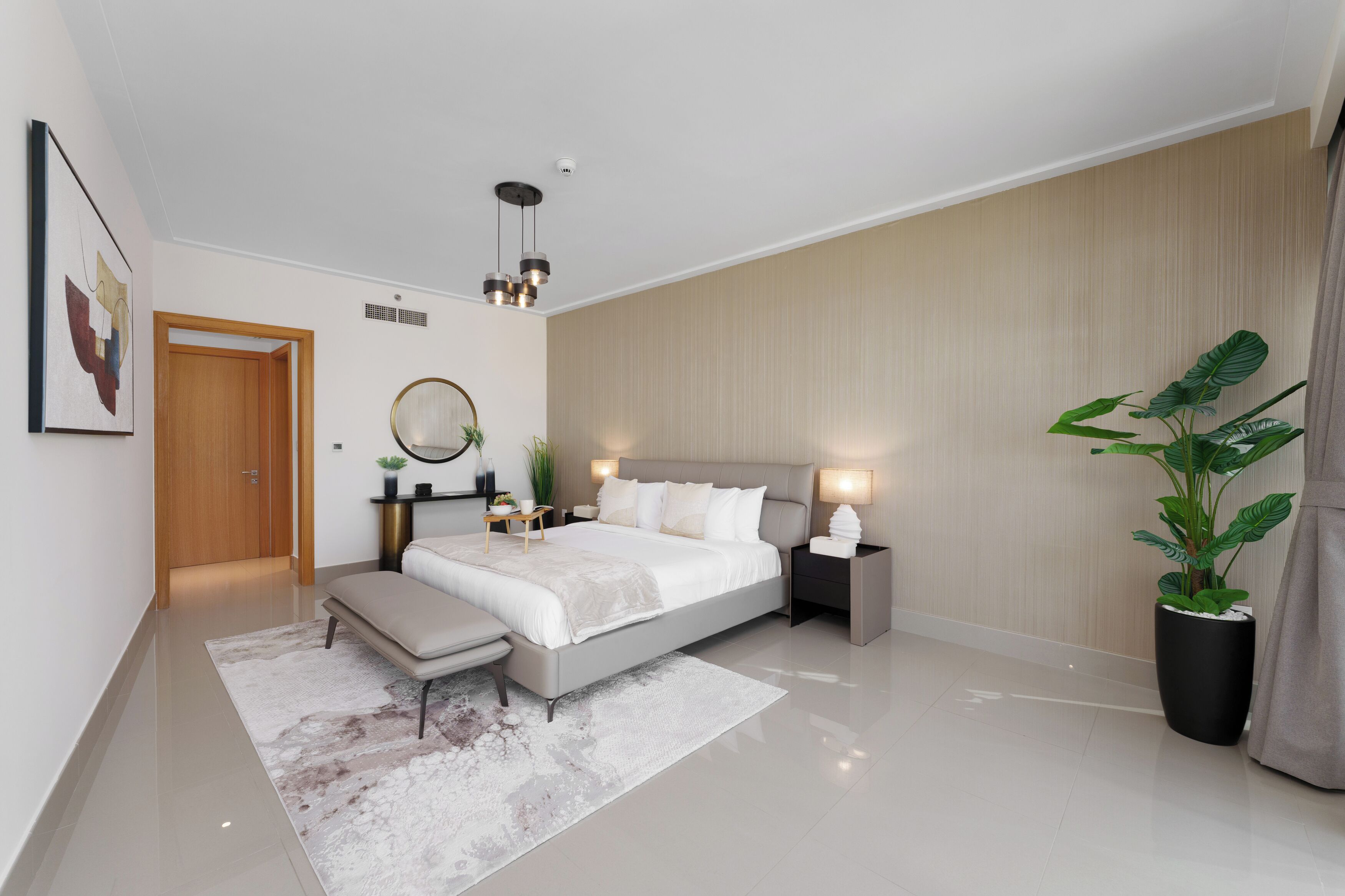 A modern bedroom with a large bed, bedside tables, a bench, a potted plant, and a ceiling light fixture.