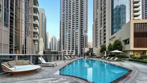 A swimming pool with lounge chairs and a sunbed, surrounded by high-rise buildings. - Maison Privee - Ultimate Living with Front-Row Views of Burj Khalifa & Dubai Fountains (Dubai)