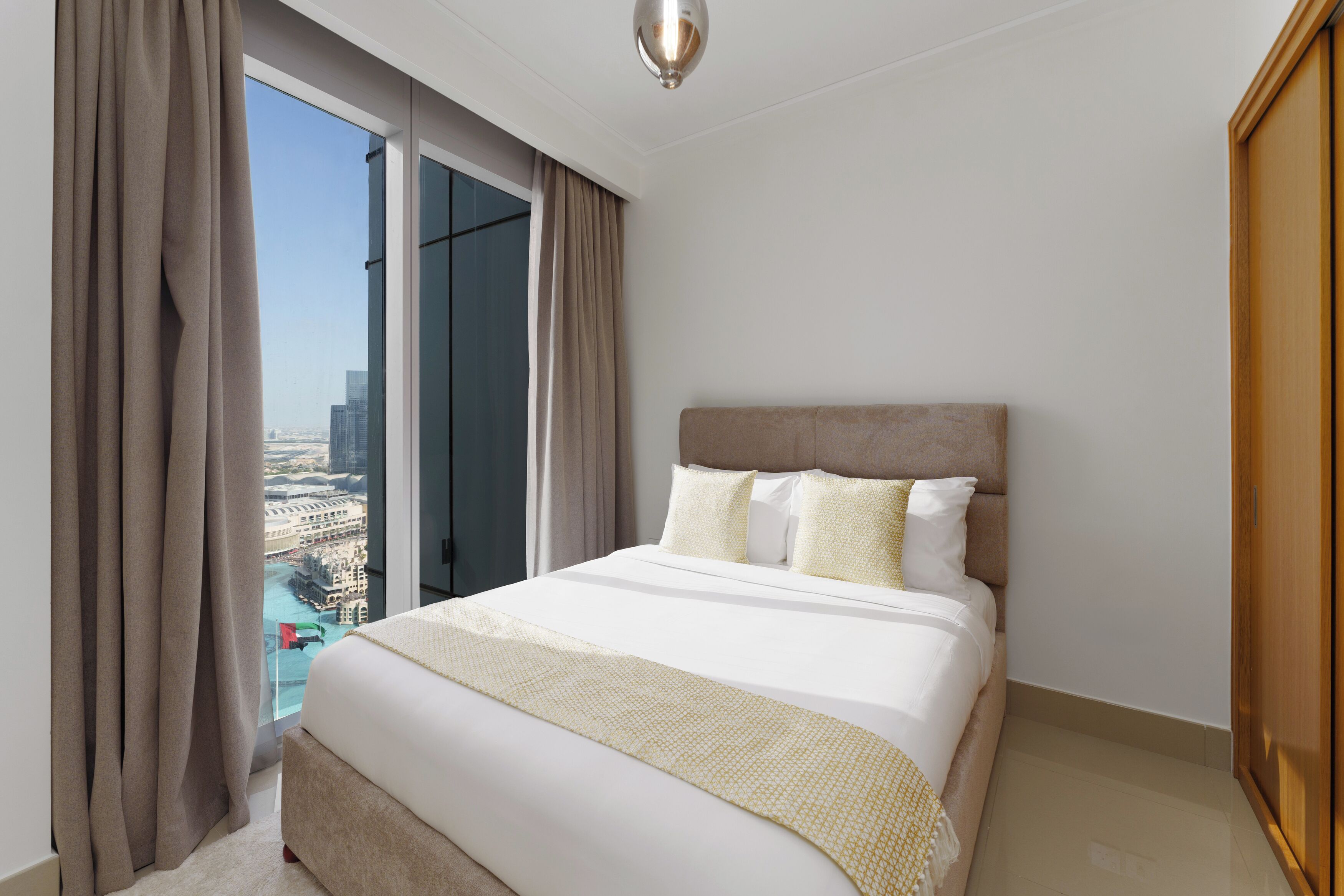 Habitación de hotel con una cama grande, vistas de la ciudad a través de un ventanal de pared a techo y una lámpara de araña moderna.