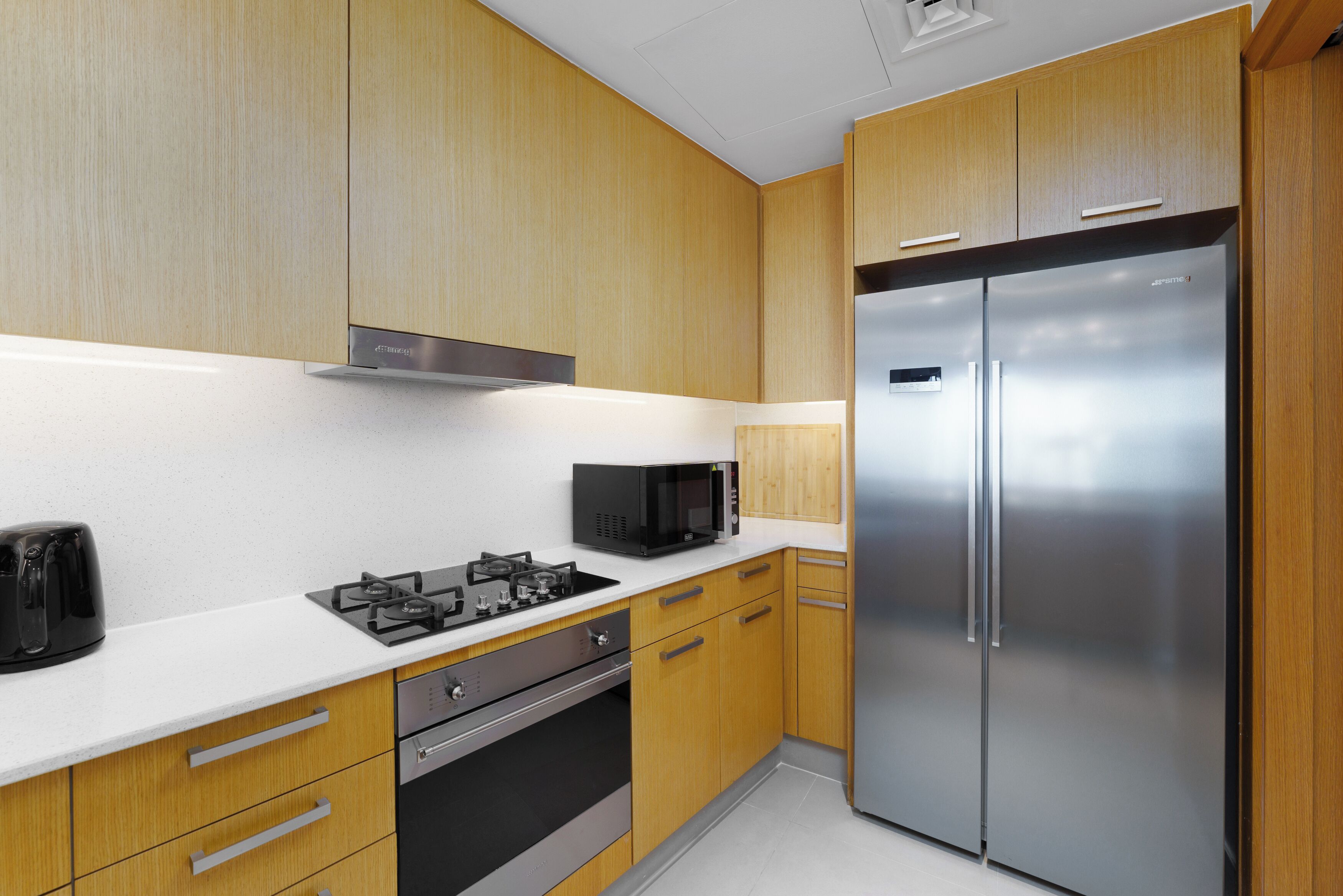 Una cucina moderna con mobili in legno, un frigorifero in acciaio inossidabile, un forno a microonde e un piano cottura a gas.