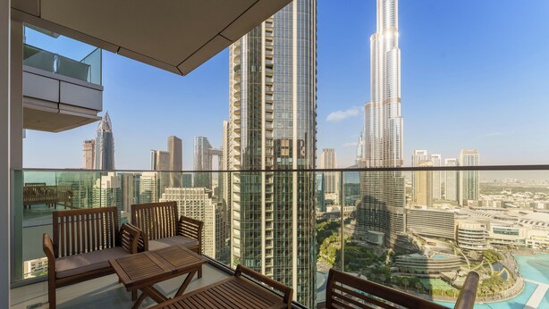 A balcony with wooden furniture, a glass railing, and a view of the Burj Khalifa and surrounding cityscape. - Maison Privee - Ultimate Living with Front-Row Views of Burj Khalifa & Dubai Fountains (Dubai)