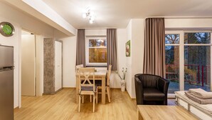 Ein modernes Wohnzimmer mit Essbereich, einer schwarzen Ledersofa, einem Holztisch und einem großen Fenster mit Vorhängen.