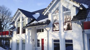 Ein zweigeschossiges Haus mit roter Tür, großen Fenstern und einem geneigten Dach.