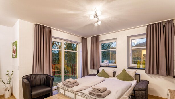 Ein Schlafzimmer mit zwei Betten, einem Sessel, einem Tisch und einem Fenster mit Vorhängen.