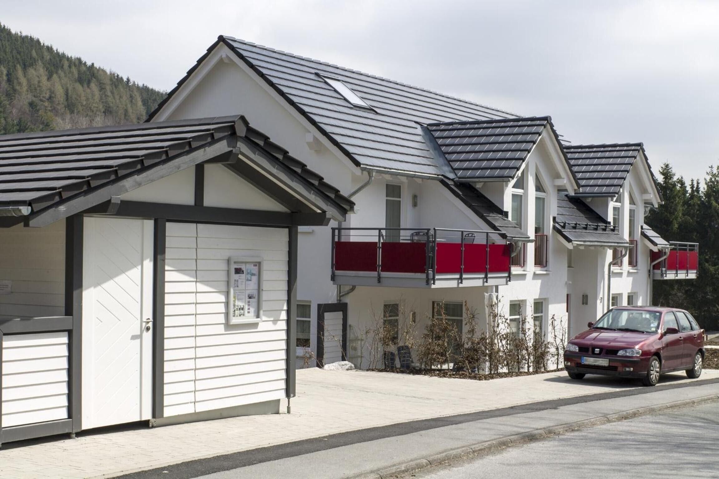 Um edifício moderno com garagem, área externa coberta e um carro estacionado.