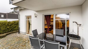 En terrasse med et bord, stole, grill og udsigt ind til et rum med spiseplads.