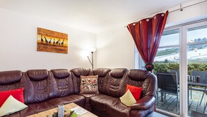 En brun lædersofa med røde og beige puder, et træbord, et billede af giraffer og udsigt til et snelandskab gennem en glasdør.