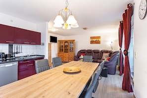 A modern kitchen with red cabinets, a wooden dining table, and a chandelier.