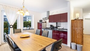 Et moderne køkken med spiseplads, et træbord, stole og udsigt til grønne omgivelser.