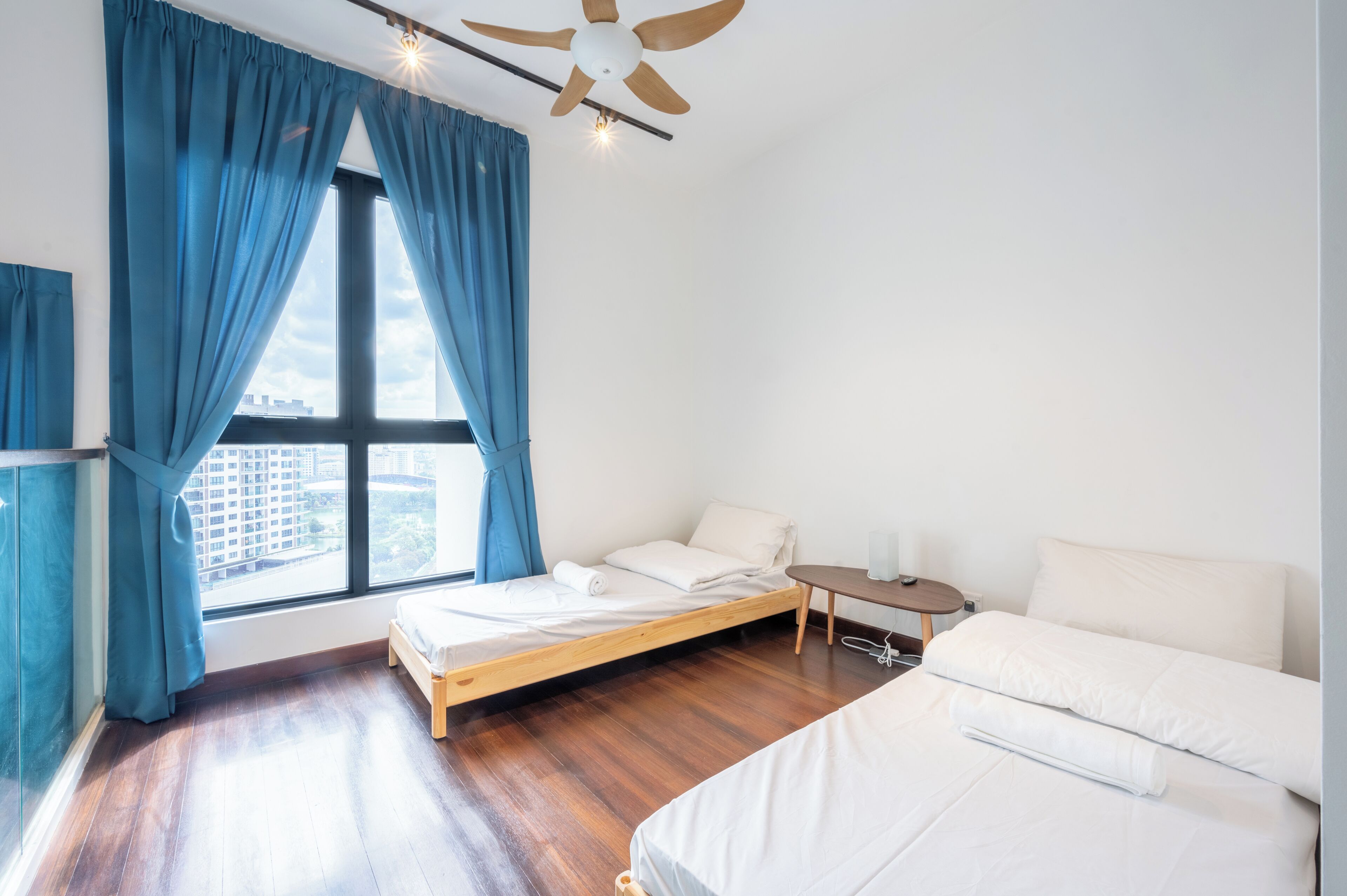 A modern hotel room with a wooden bed, a small bedside table, a white sofa, and a large window with curtains.