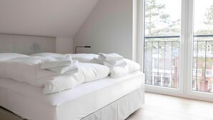 Ein ordentlich bezogenes Bett in einem Zimmer mit einem großen Fenster und Blick auf Gebäude.