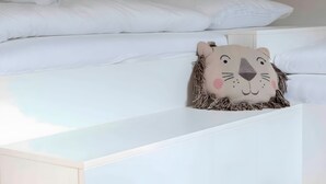 Een moderne slaapkamer met een wit bed, een zacht kussen in dieren vorm en een witte nachtkastje.