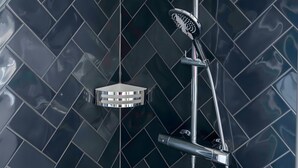 Een douche met een handdouche en een wandgedouche, beide met chroomafwerking, tegen een donkere betegelde muur.