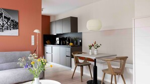 Un salon moderne avec un canapé, une table à manger et des chaises, une cuisine en arrière-plan et un luminaire suspendu.
