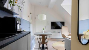 A modern kitchen with a black refrigerator, a dining area with a white table and chairs, a TV mounted on the wall, and a round rug on the floor. - Apartment 'Ocean Star' with Balcony and Wi-Fi (Sankt Peter-Ording)