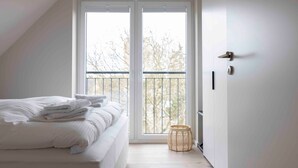 A bedroom with a bed, a window with a view, and a door. - Apartment 'Ocean Star' with Balcony and Wi-Fi (Sankt Peter-Ording)