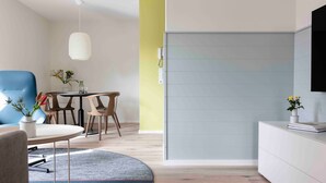 Une pièce moderne avec une table ronde, des chaises, un fauteuil bleu, un meuble blanc et un téléviseur fixé au mur.