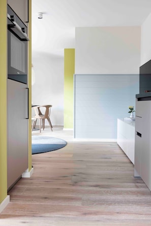 A modern kitchen with a built-in oven, a dining area with a round table and chairs, and a light-colored wall with a vertical stripe. - Apartment 'Viking' with Balcony and Wi-Fi (Sankt Peter-Ording)