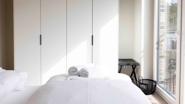 Une chambre à coucher avec un lit, une armoire, une petite table et une fenêtre donnant sur un paysage agréable.
