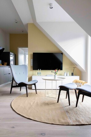 Ein modernes Wohnzimmer mit Fernseher, Sitzgelegenheiten und einer Küche im Hintergrund.