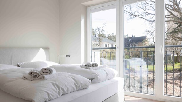 A bedroom with a large bed, a view of the outdoors through a sliding glass door, and a balcony with a railing. - Apartment 'Sunseeker' with Balcony and Wi-Fi (Sankt Peter-Ording)