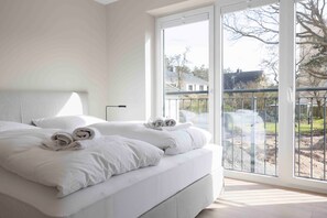 Une chambre dotée d’un grand lit, offrant une vue sur l’extérieur grâce à une porte-fenêtre coulissante, et d’un balcon avec une balustrade.