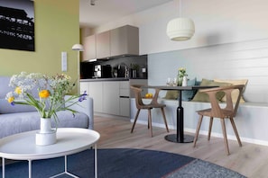 Un salon moderne avec un canapé, une table à manger et des chaises, une cuisine en arrière-plan et un vase rempli de fleurs posé sur une table d’appoint.