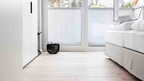 A room with a sliding glass door, a bed with white bedding, a black woven basket, and a view of a building outside. - Apartment 'Invictus' with Private Terrace and Wi-Fi (Sankt Peter-Ording)