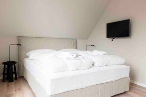 Un lit bien fait dans une pièce dont le plafond est en pente et où un téléviseur est fixé au mur.