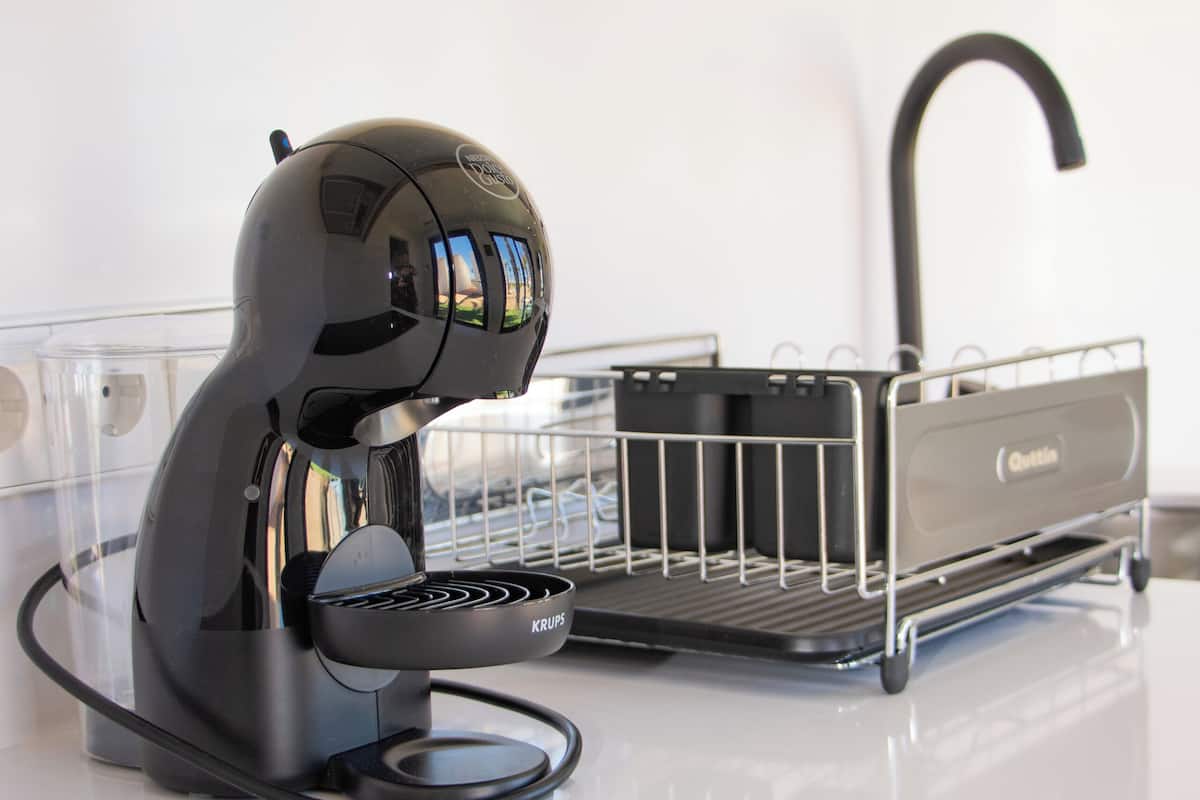 A coffee machine with a Krups brand, a metal basket, and a clear glass container on a white countertop.