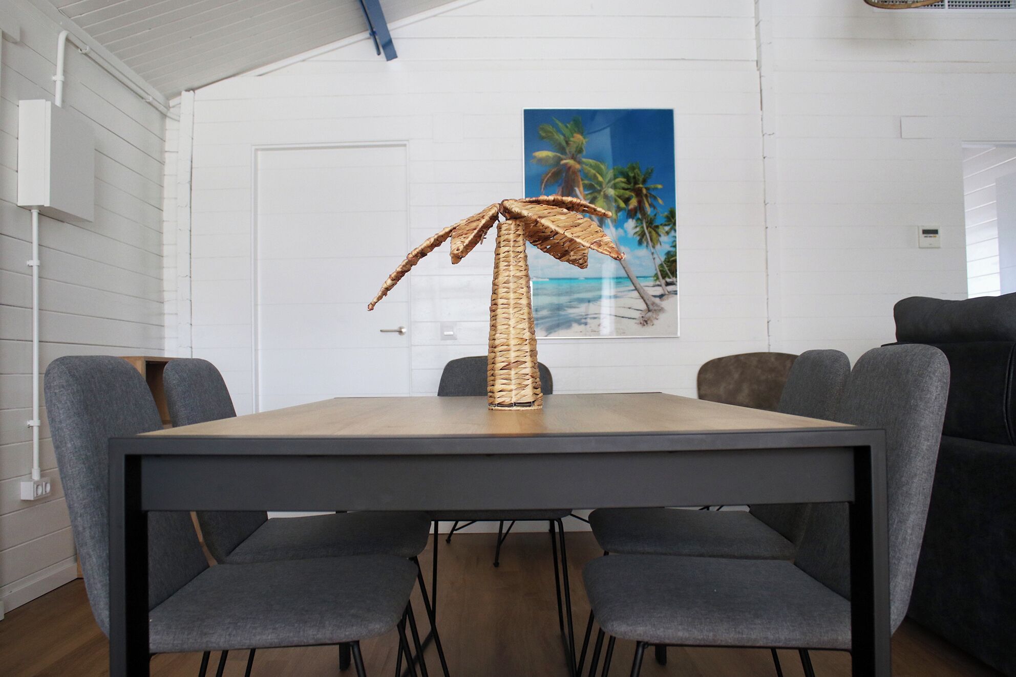 Un comedor con una mesa y sillas, una planta decorativa y un cuadro de una playa en la pared.