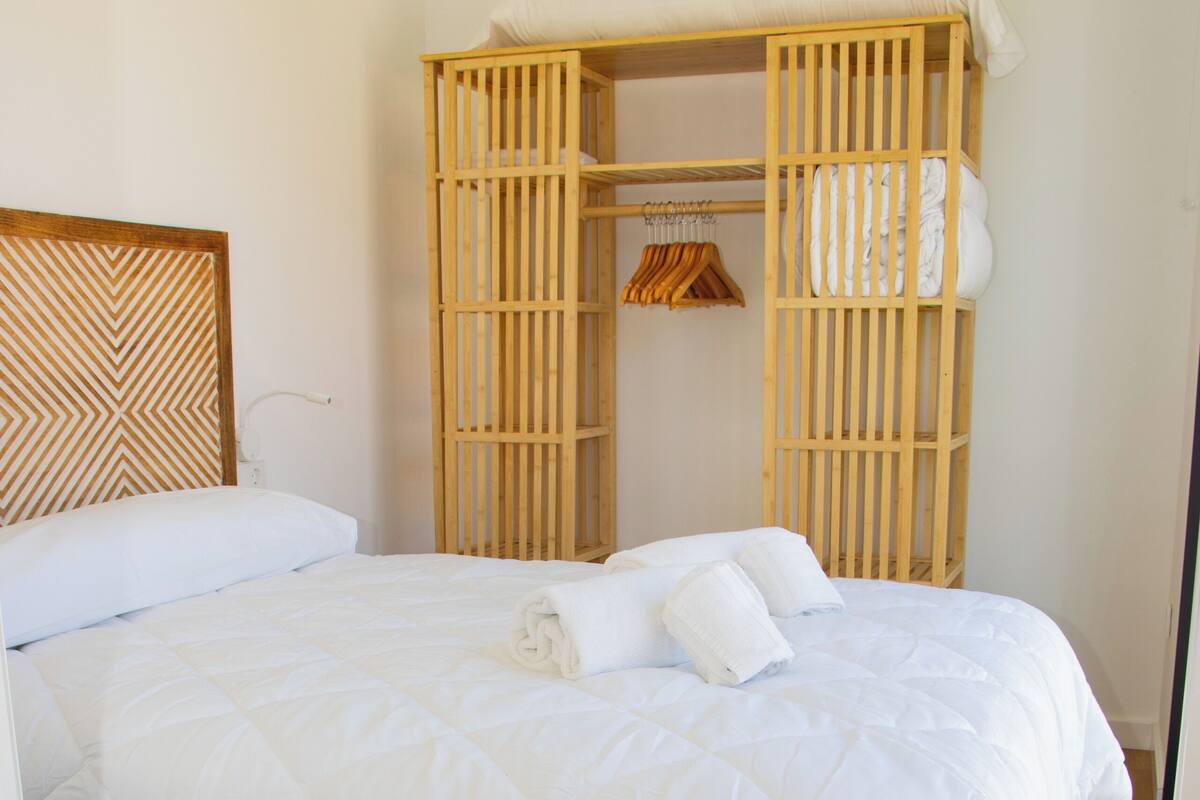 A neatly made bed with white bedding, a wooden headboard, and a wooden crib attached to the wall.