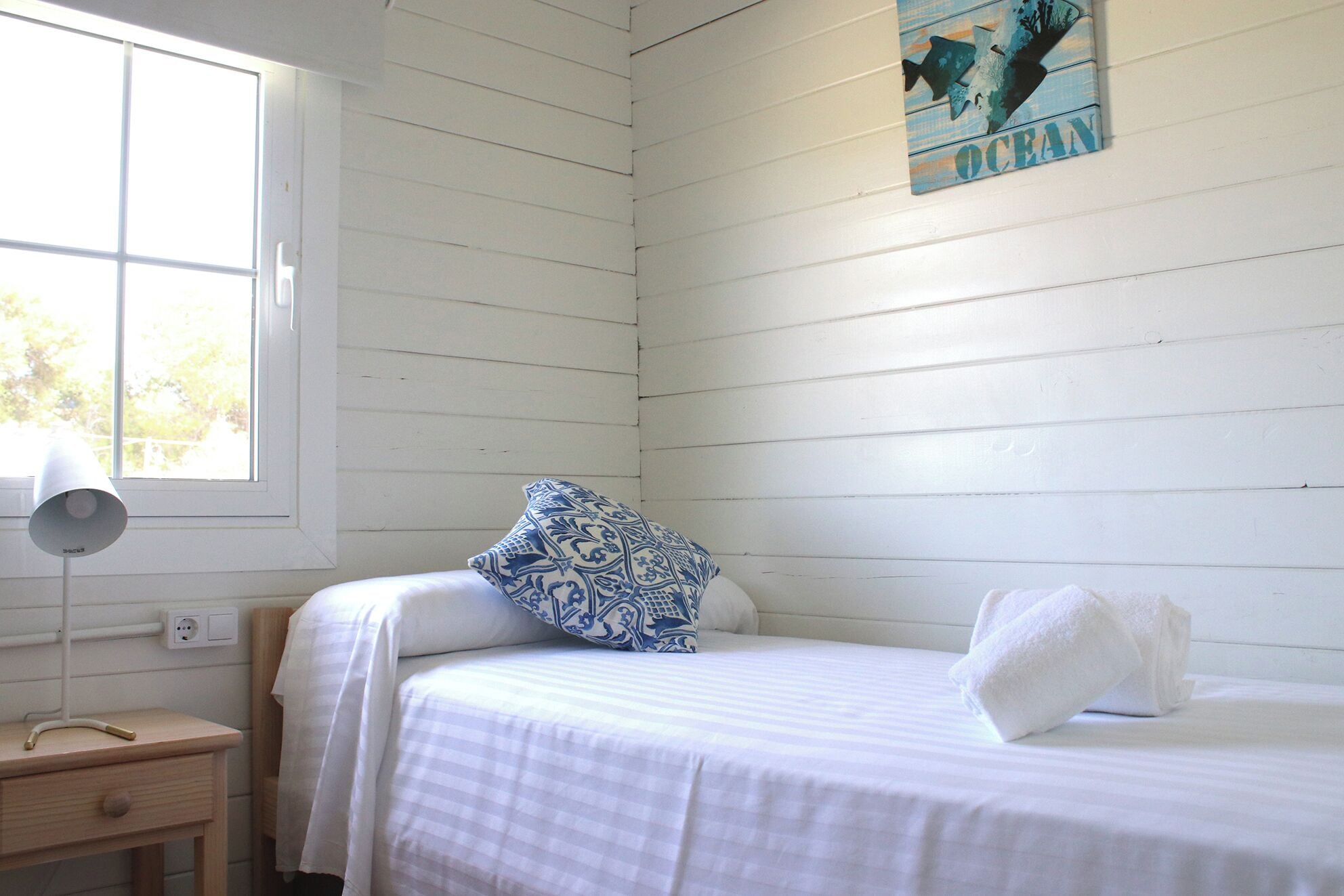Un dormitorio con una cama, una mesita de noche, una lámpara y una ventana.