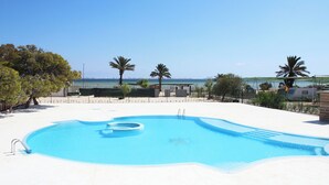 En swimmingpool med fri utsikt över havet, omgiven av palmer och en sandstrand.