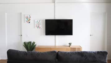 A living room with a black sofa, a wooden coffee table, a flat-screen TV mounted on the wall, and two wall-mounted pendant lights.