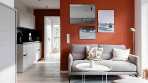 A modern living room with a grey sofa, a round coffee table, and a kitchen in the background. - Apartment 'Quicksilver' with Balcony and Wi-Fi (Sankt Peter-Ording)