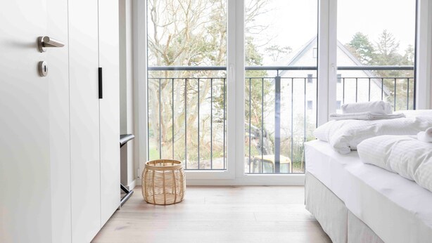 A bedroom with a large window, a balcony, a bed, and a wicker basket. - Apartment 'Quicksilver' with Balcony and Wi-Fi (Sankt Peter-Ording)