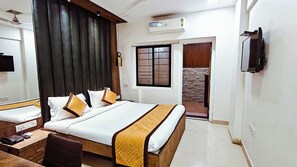 Habitación de hotel con una cama grande, un escritorio con silla, un televisor montado en la pared y una ventana con vista a un muro de piedra.