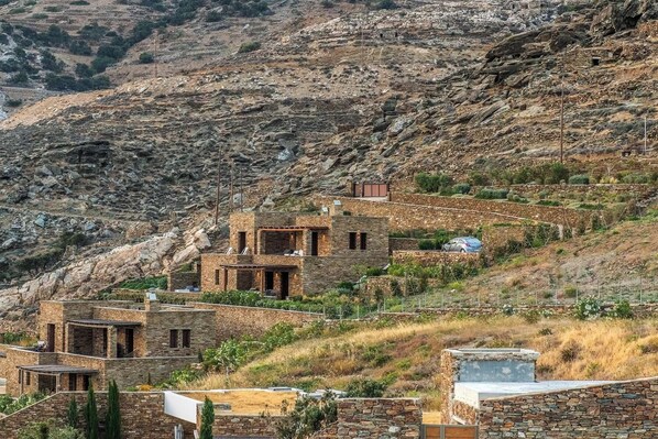 A stone building with multiple rooms, situated on a hillside with rocky terrain and sparse vegetation. - Dolce Villa Tinos Kardiani in Stone & Sunset Views (Kardiani)