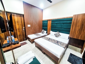 A hotel room with two beds, wooden paneling, a green upholstered headboard, and a small desk with a computer and water bottles. - Hotel Anjana Cottage (Amritsar)