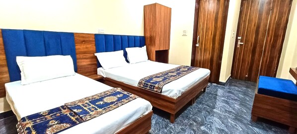 A hotel room with two single beds, a wooden wardrobe, a small wooden table, and a blue carpeted floor. - Hotel Anjana Cottage (Amritsar)