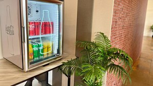 A minibar with a refrigerator containing Coca-Cola and Schweppes cans, a bottle of orange juice, and a bottle of water.