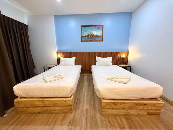 Une chambre d’hôtel avec deux lits, des têtes de lit en bois, une table de chevet, un tableau au mur et un rideau.