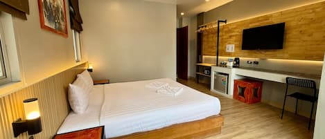 A modern hotel room with a large bed, a desk, a TV, and a small kitchenette.