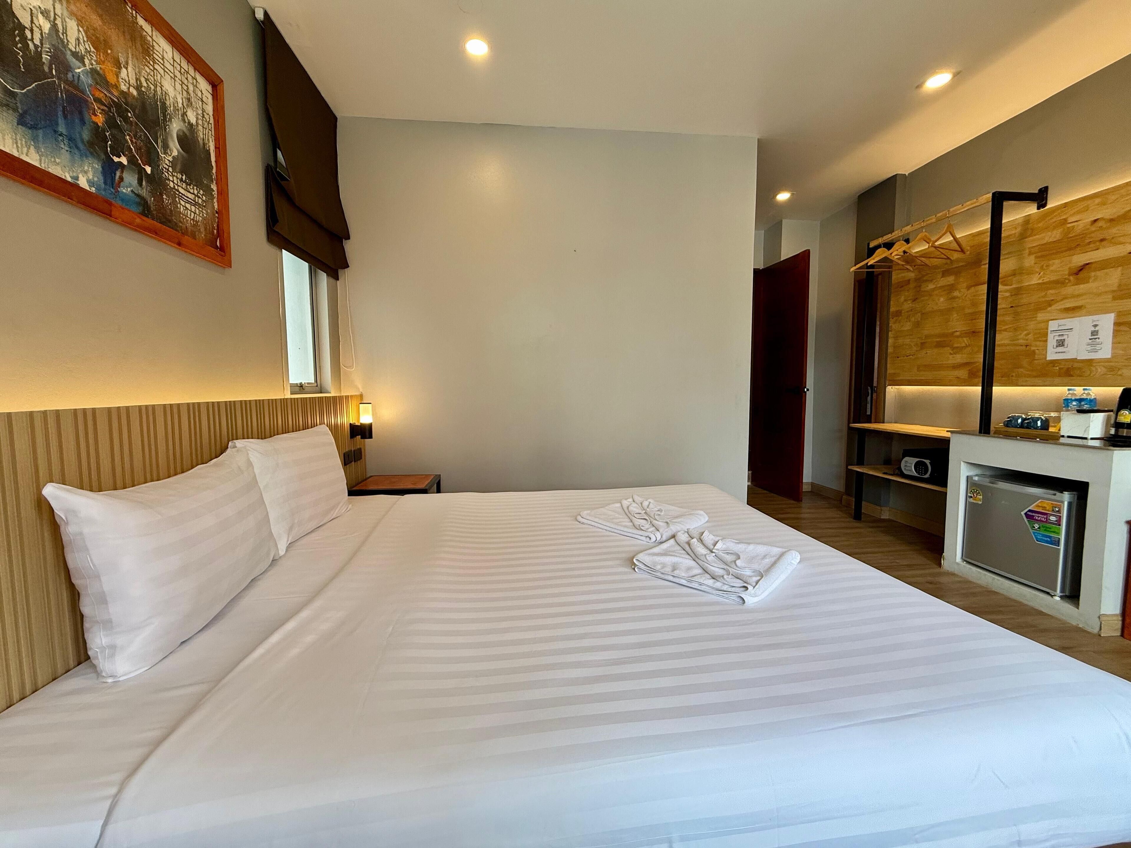 A hotel room with a large bed, a desk with a refrigerator, a mirror, and a painting on the wall.