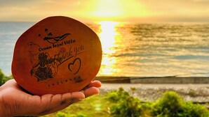 A hand holding a round object with text and a map, with a sunset and ocean in the background. - Ocean Front Villa (Hikkaduwa)