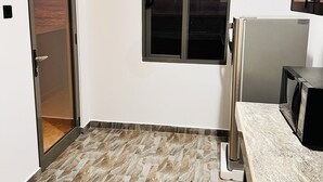 A compact kitchen with a built-in refrigerator, a microwave, and a window with a sunset view. - Ocean Front Villa (Hikkaduwa)