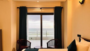 A hotel room with a bed, two chairs, a small table, and a view of the ocean. - Ocean Front Villa (Hikkaduwa)